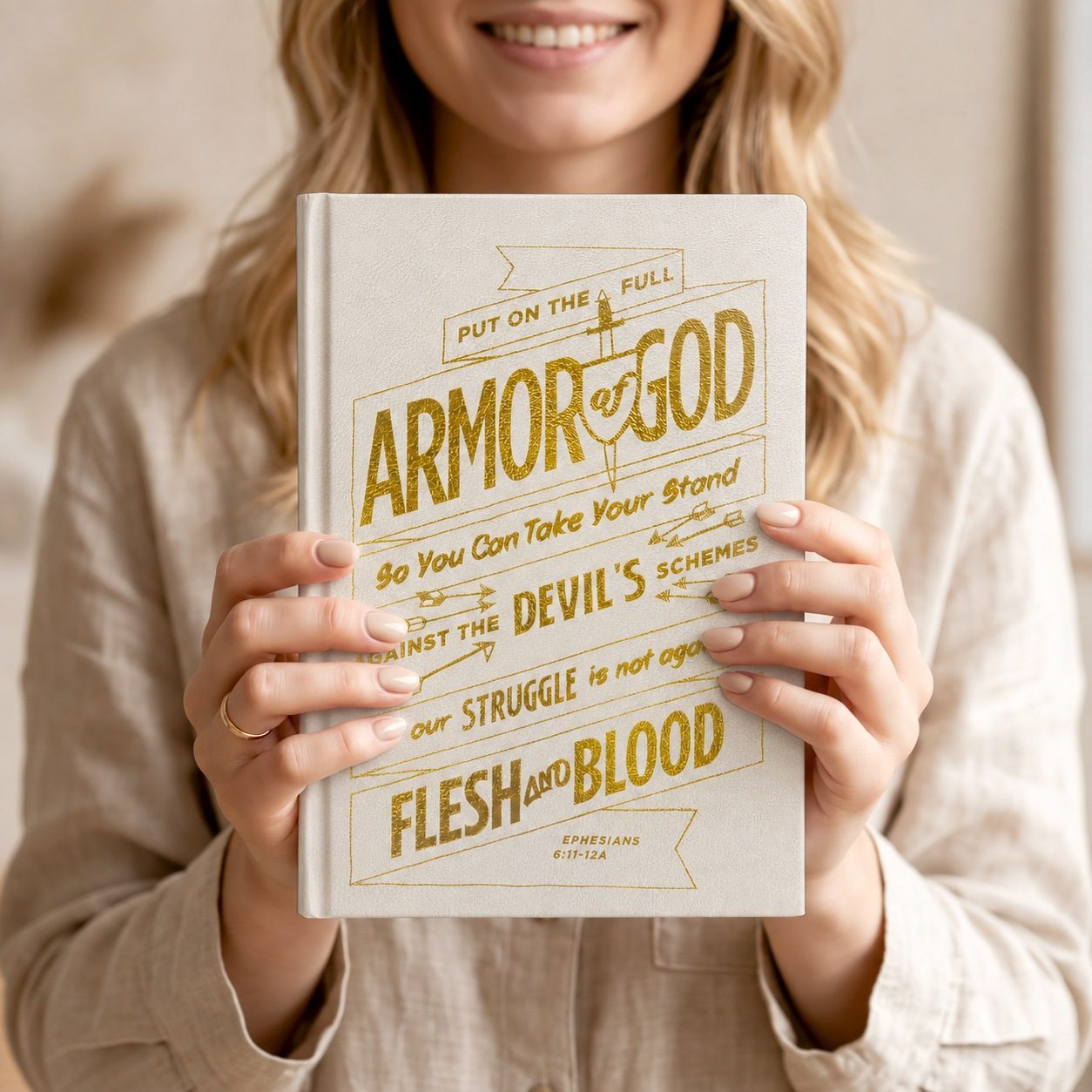 A woman smiling and holding a white Gospelis Armor of God journal with gold foil lettering
