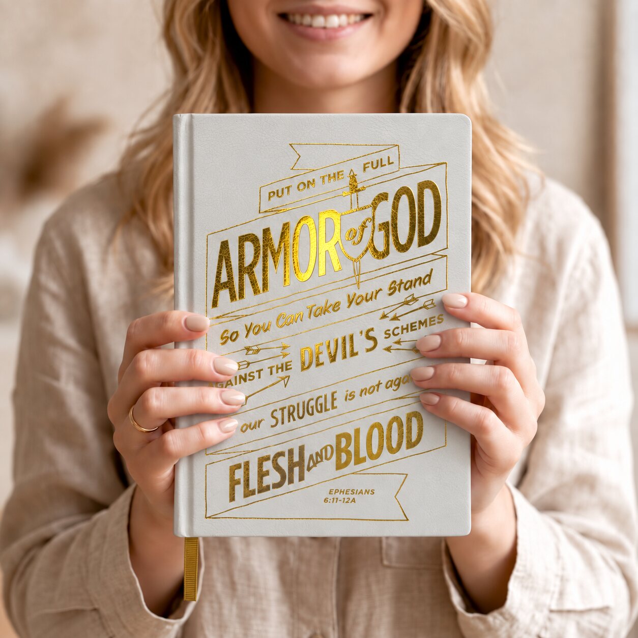 A woman smiling and holding the real white Gospelis Armor of God journal with gold foil lettering